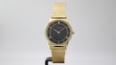 Front view of the gold Limit watch with black dial and mesh bracelet on a stand.