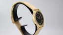 Other angled side view of the gold Limit watch case and mesh bracelet on a black stand.