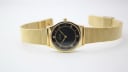 Top-down view of the gold Limit watch with black dial and mesh bracelet laid flat.