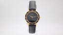 Front view of the Amara watch with a gold-tone case and a plain black dial, featuring gold Roman numerals on the bezel and a black leather strap.