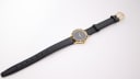 Overhead view of the Amara watch and its full-length black leather strap with a gold-tone buckle.