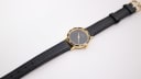 Full overhead view of the Amara watch, displaying the black leather strap and gold-tone buckle against a white background.