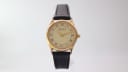 Full front view of the Rodania 18711 watch on a display stand, showcasing its round gold case and black leather strap.
