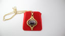 Front view of the Oris gold-tone pendant watch with black oval dial, resting on a red velvet pad with its integrated chain.