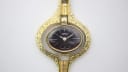 Face-on view of the Oris gold-tone pendant watch, highlighting the unique case texture and black dial.