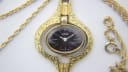 Oris gold-tone pendant watch on a red velvet pad, with the integrated chain loosely arranged beside it.