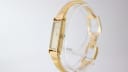 Angled view of the Gucci 1500L watch, showing the crown and integrated gold tone bracelet on a display stand.