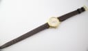 Top-down view of the Slava watch with its brown leather strap extended flat.
