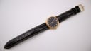 Full length view of the Ingersoll watch with its black leather strap and gold-tone buckle laid flat.