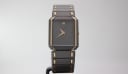 Front view of Seiko 5470-7000 rectangular two-tone watch with black dial and gold-tone hands on a stand.