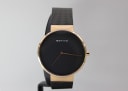 Front view of the Bering watch with a black dial, gold-tone case, and black mesh bracelet on a stand.