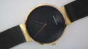 Slightly wider close-up of the minimalist black dial, gold-tone case, and mesh strap.