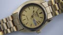 Close-up of the gold-tone dial with baton indices, Seiko 5 logo, day-date window, and 'automatic' text.