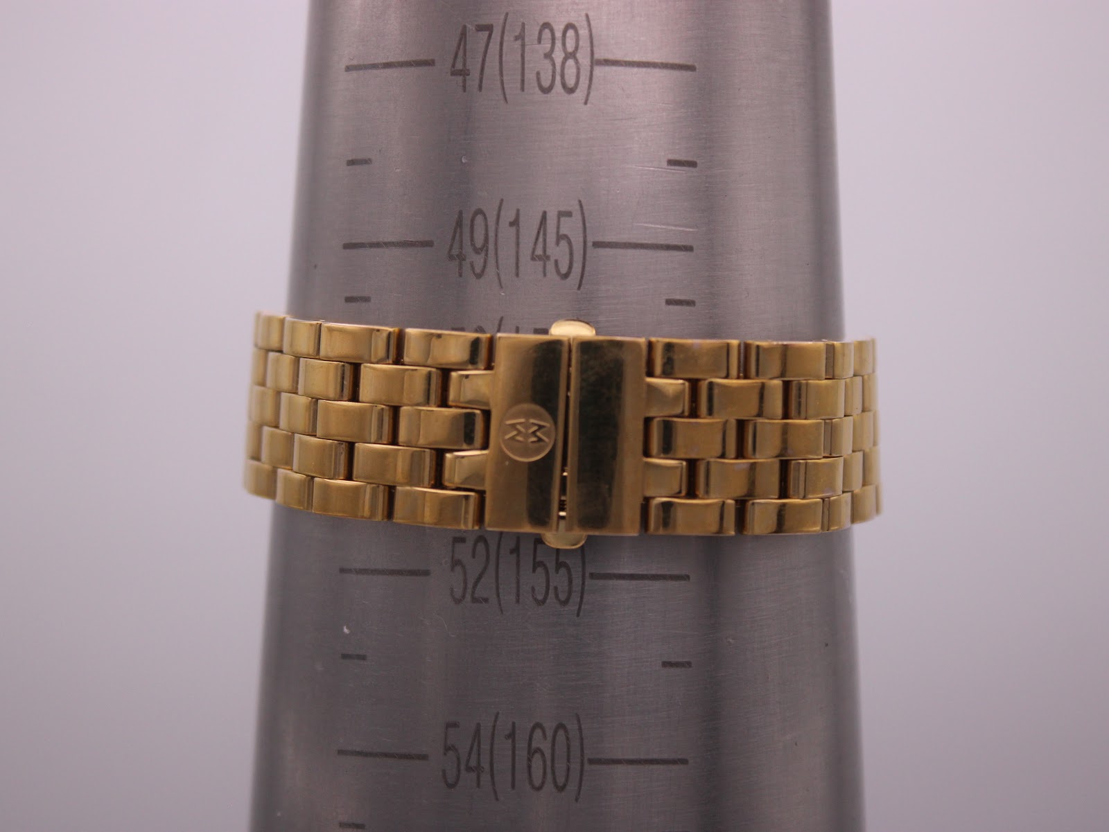 Side profile view of the gold-tone Michele watch, highlighting the diamond bezel, fluted crown with red detail, and integrated bracelet.