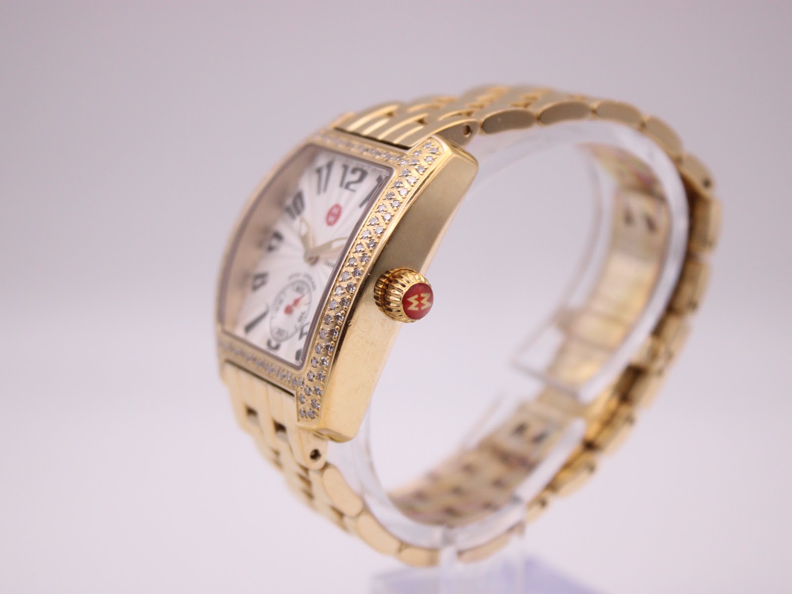Side view of the gold-tone Michele bracelet and watch case on a white background, extended flat.