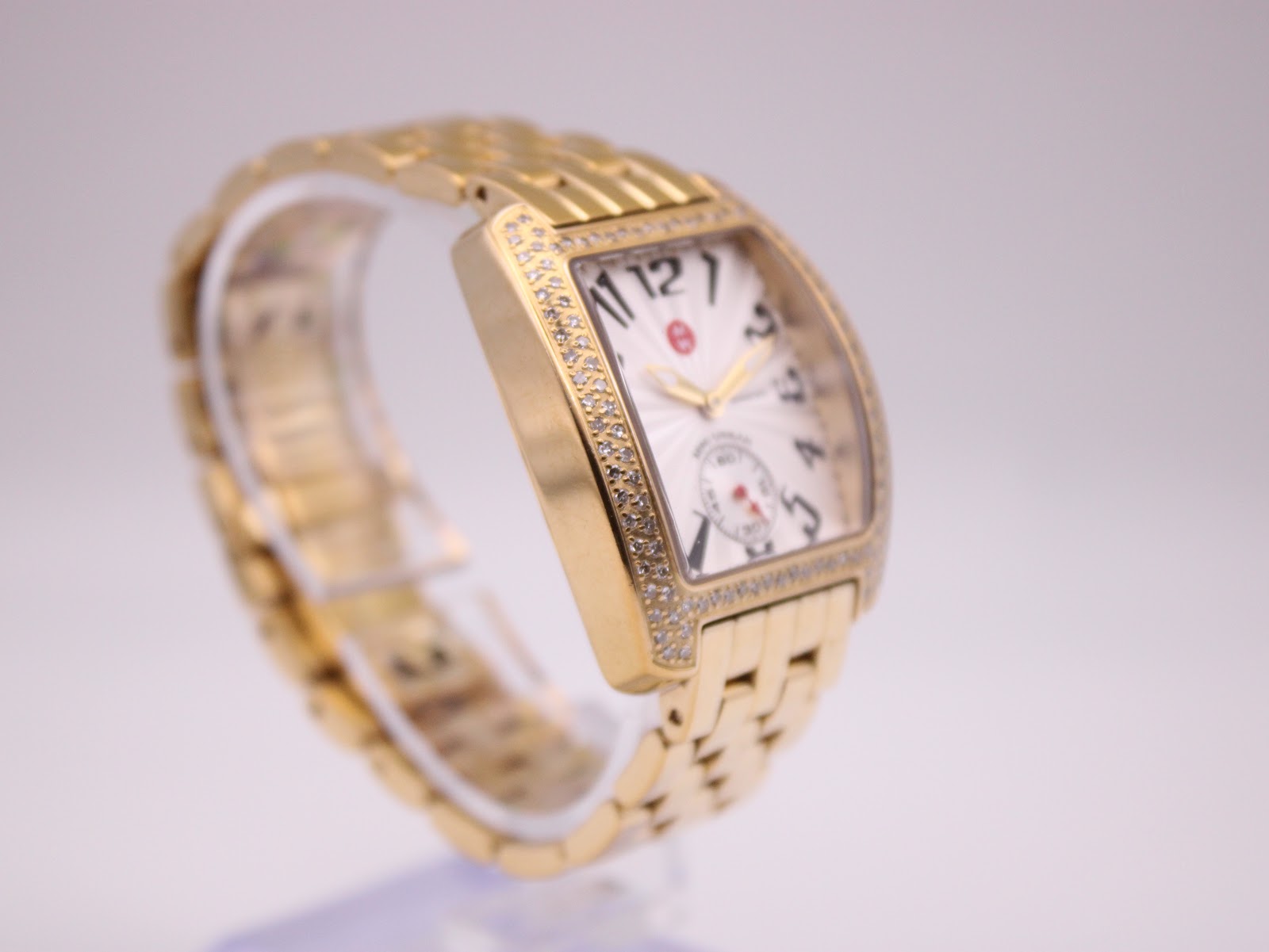 Close-up view of the gold-tone Michele bracelet links and part of the case on a white background.