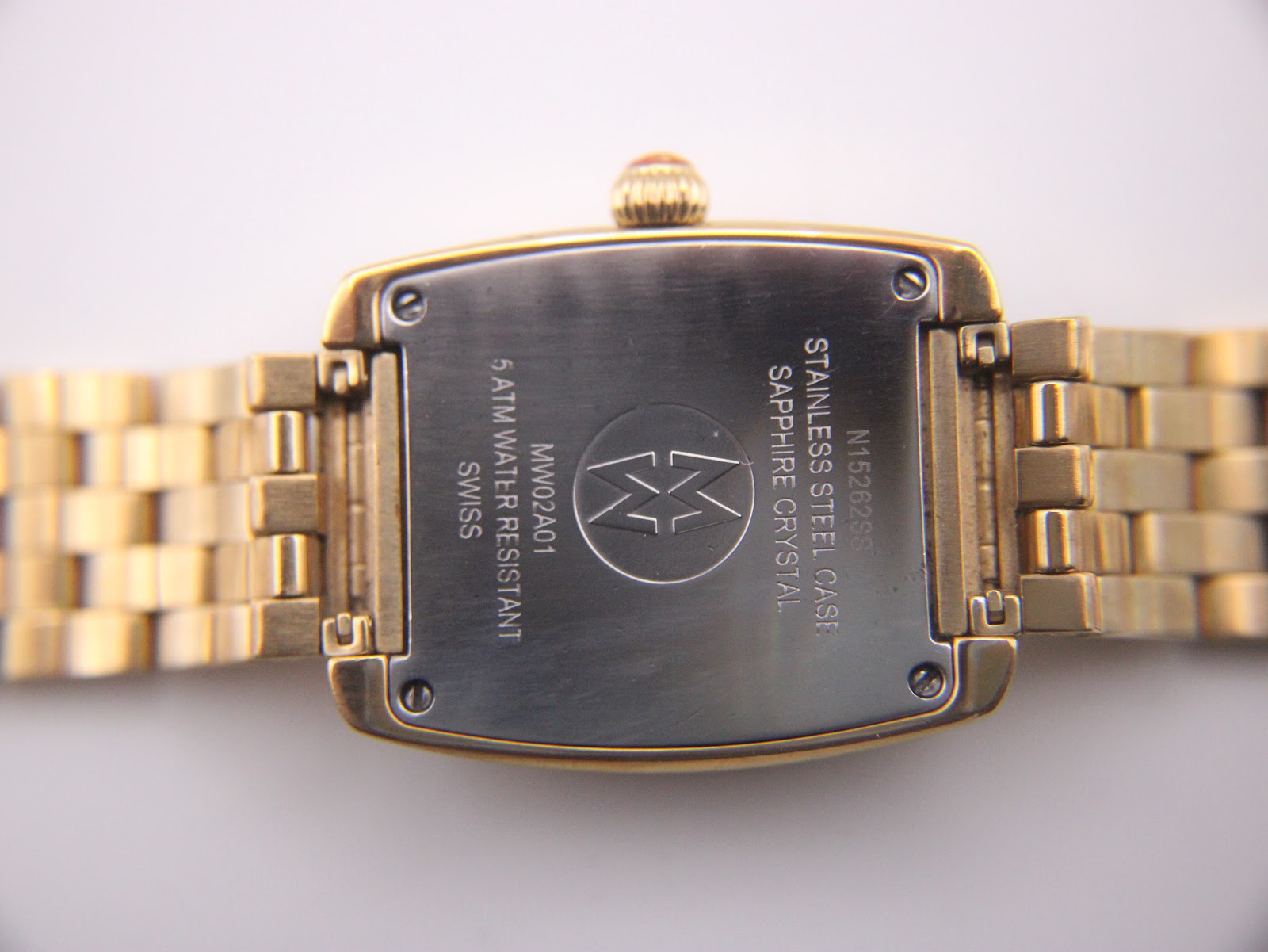 Extreme close-up of the watch crown, showing the fluted gold-tone design and the red accent with the Michele logo.