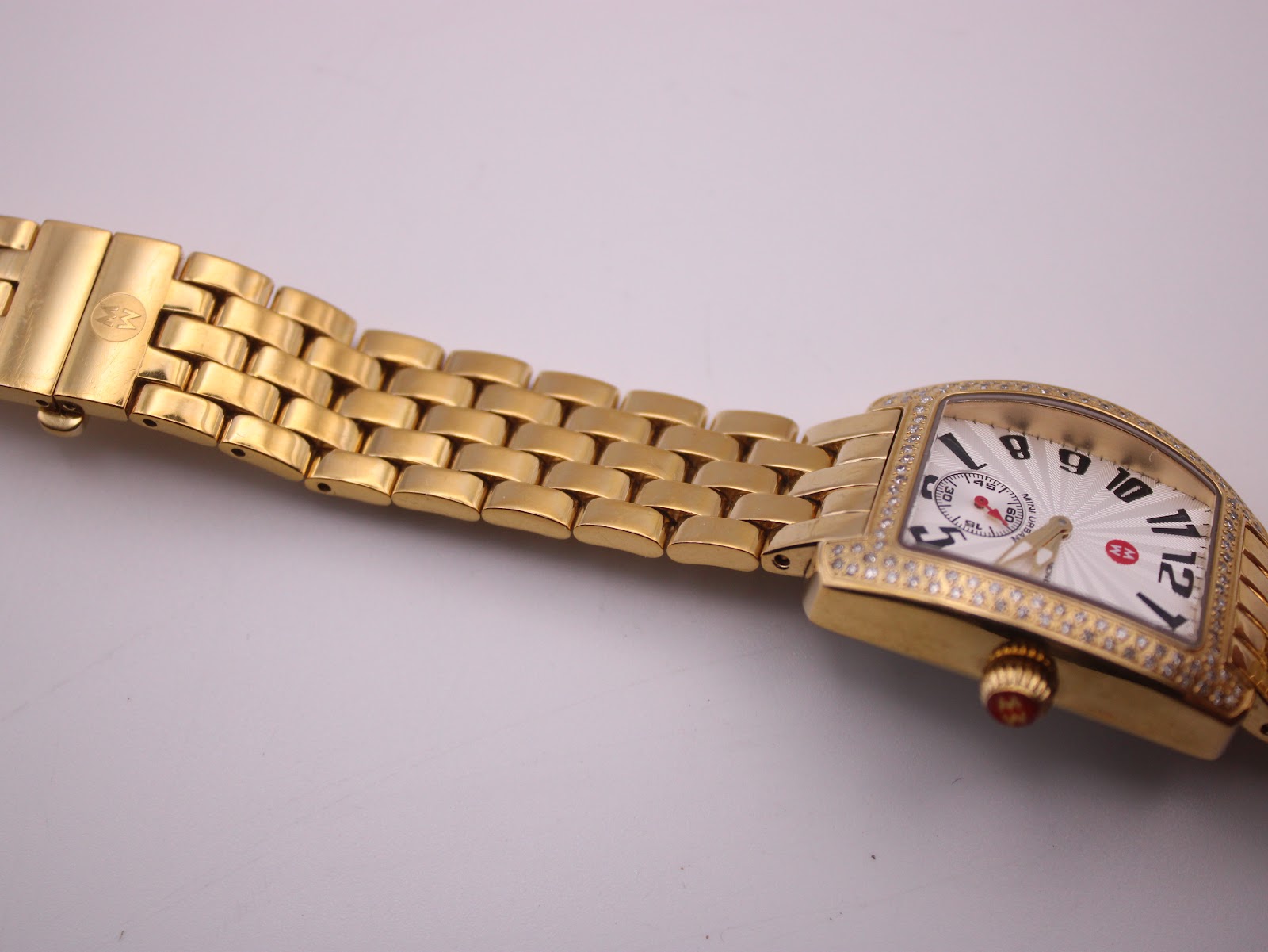 Close-up of the gold-tone Michele bracelet's deployment clasp, featuring the engraved Michele logo.
