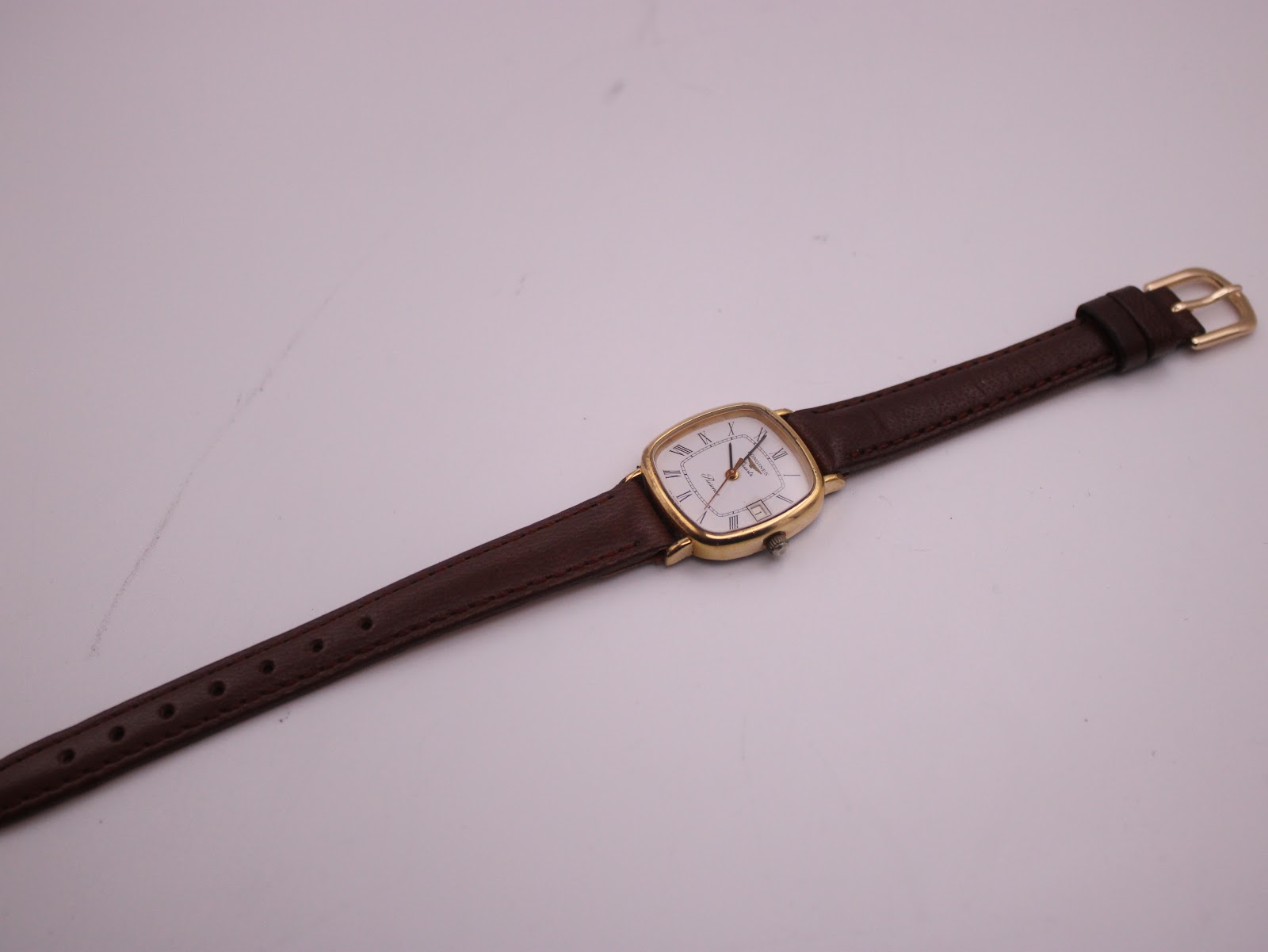 Overhead view of the Longines Presence watch laid flat, displaying the full length of the brown leather strap with gold buckle.