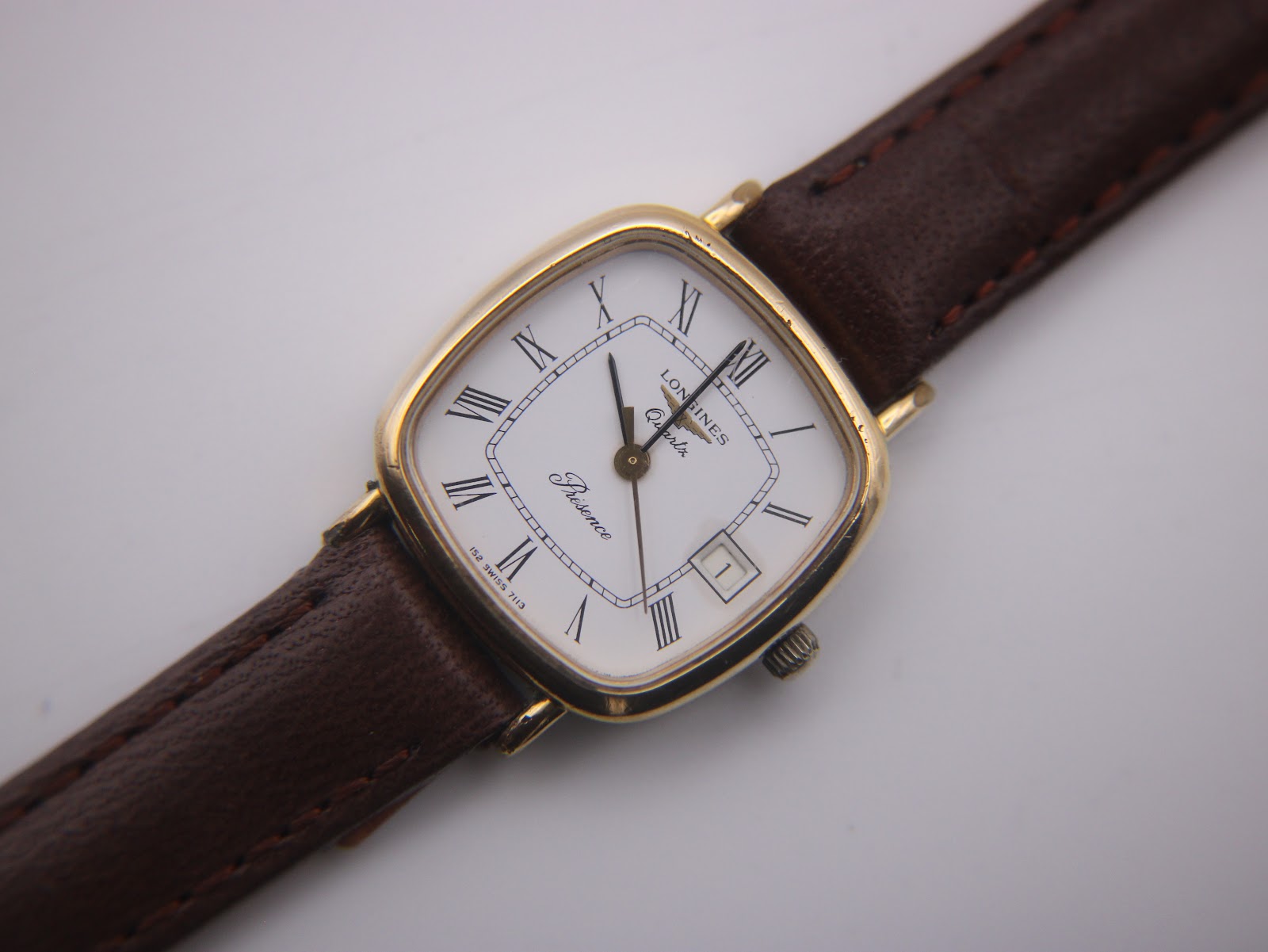 Close-up front view of the Longines Presence watch dial, detailed Roman numerals, gold hands, and date window.