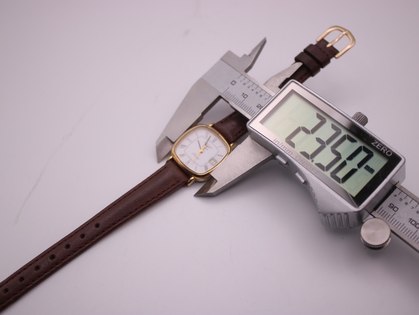 Digital caliper measuring the Longines Presence watch case, showing a precise diameter of 23.50mm.