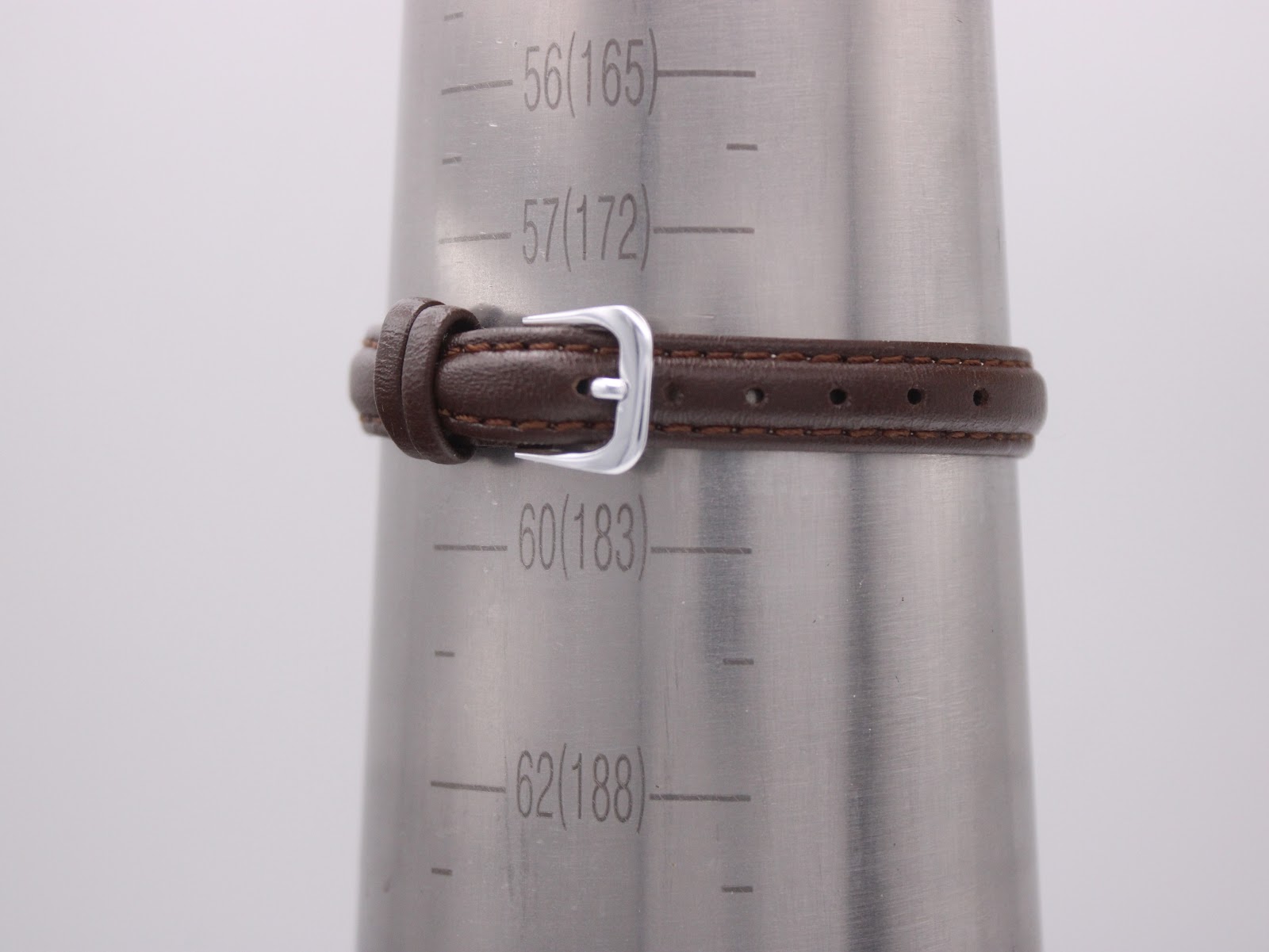 Close-up of the brown leather strap on a wrist sizing tool, showing the buckle and strap holes against the measurement scale.