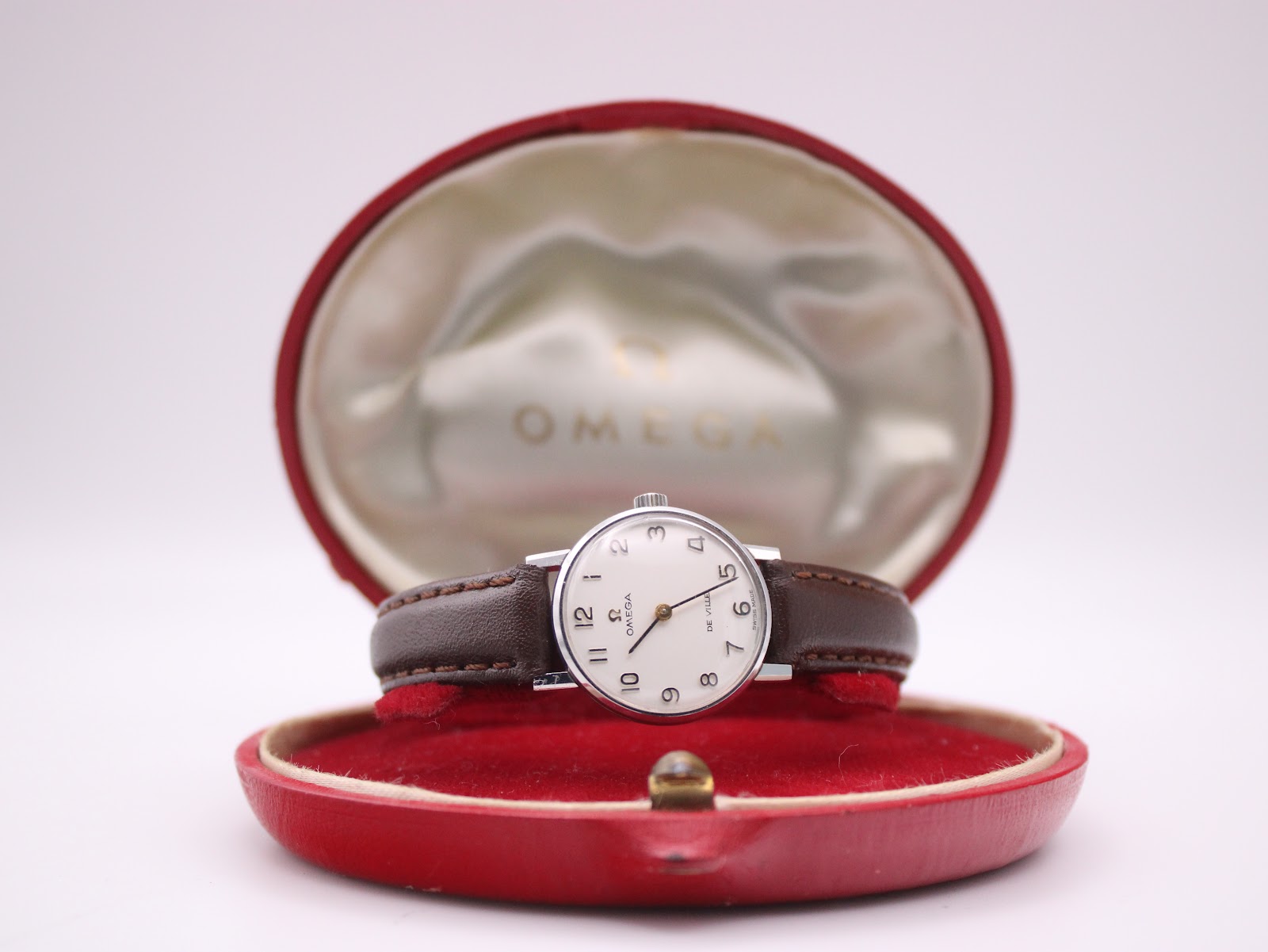 The Omega De Ville watch displayed open in its original red presentation box with a satin interior and Omega logo.