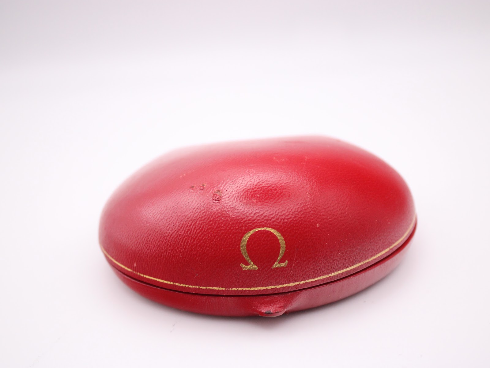 The original red Omega presentation box, closed, showing its domed shape and gold Omega logo on the lid.