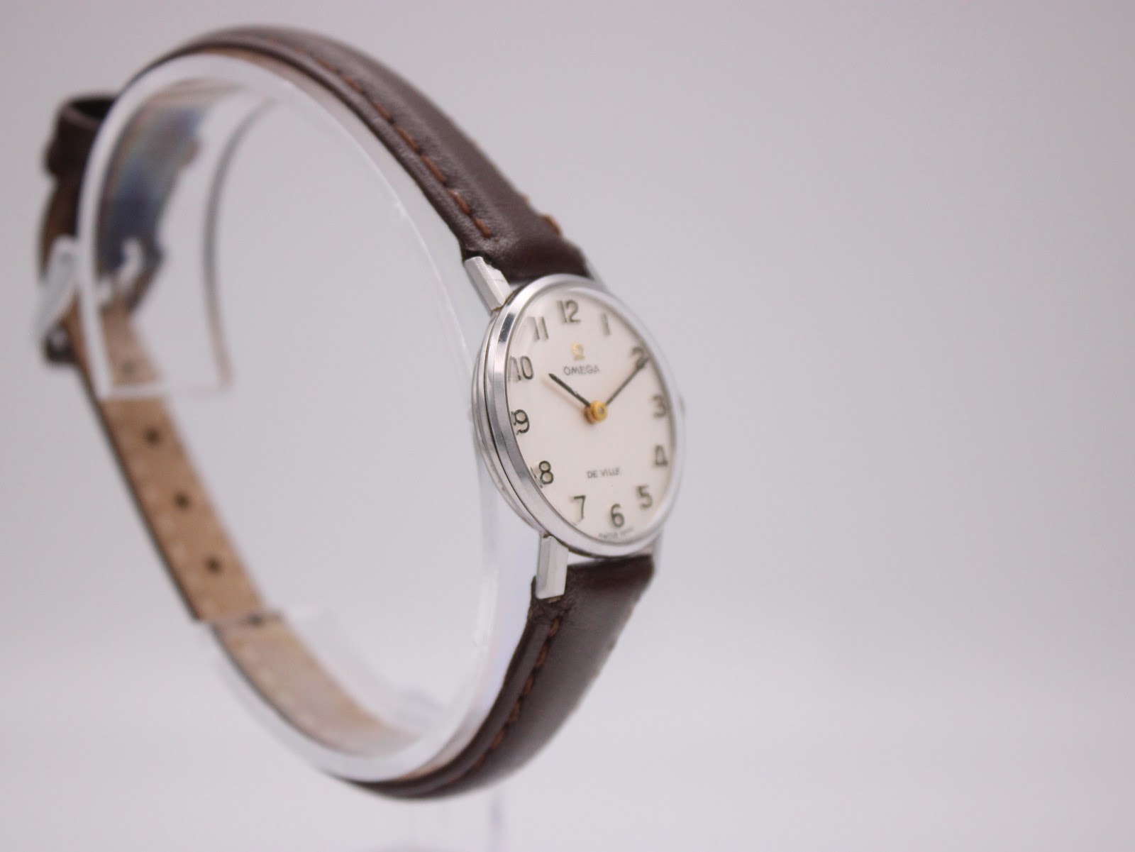 Another angled side view of the Omega De Ville watch on a stand, showing the other side of the polished case.