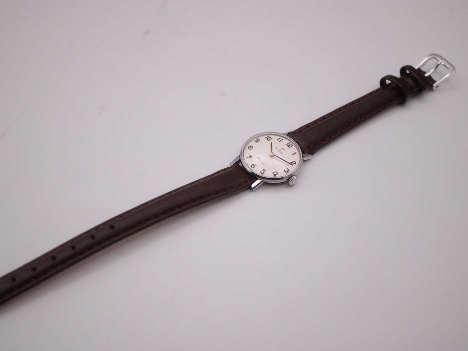 Overhead view of the full Omega De Ville watch with its brown leather strap laid flat on a white surface.