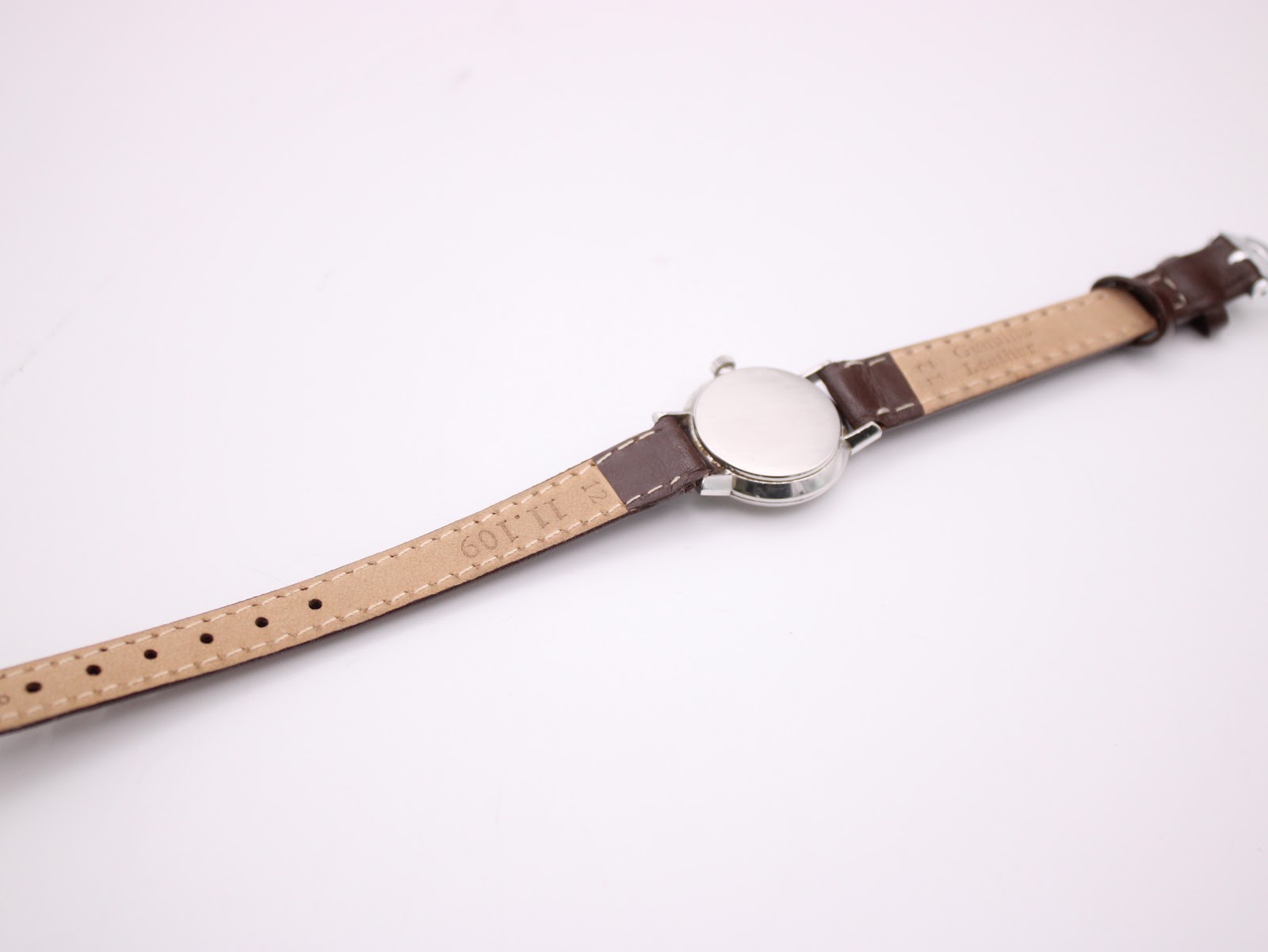 Back view of the Omega De Ville watch, showing the plain case back and the underside of the brown leather strap with 'Genuine Leather' embossed.