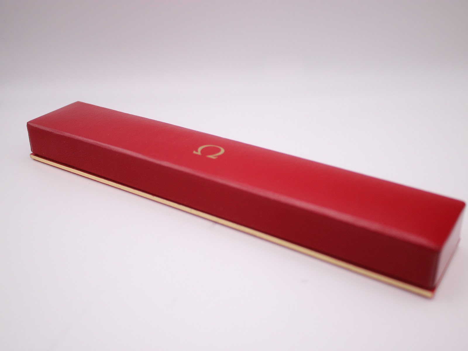Exterior view of the rectangular red original Omega watch box with a gold Omega logo.