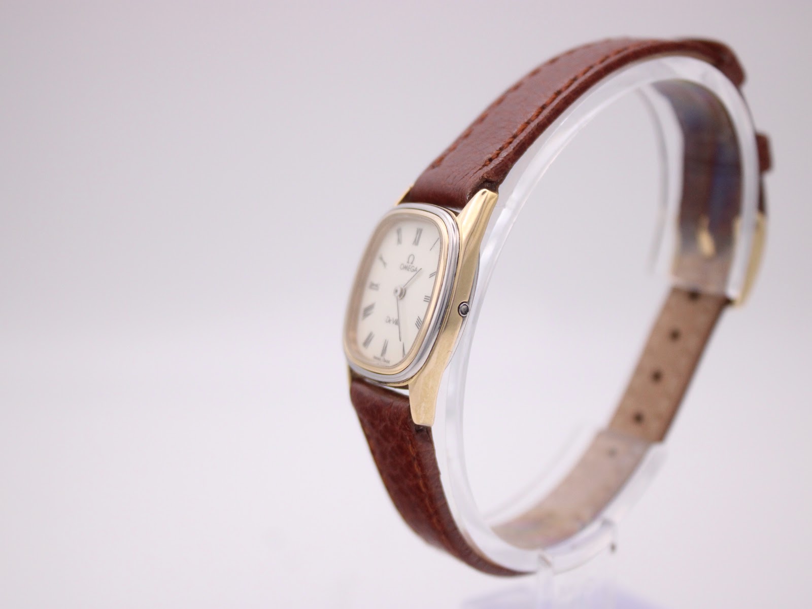 Angled side view of the Omega De Ville watch, showing the gold-plated case side and brown leather strap.