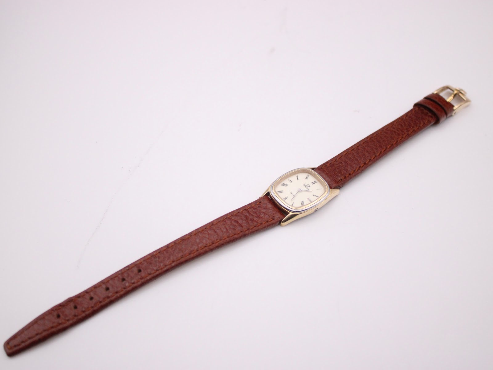Top-down view of the entire Omega De Ville watch with its brown leather strap laid flat.