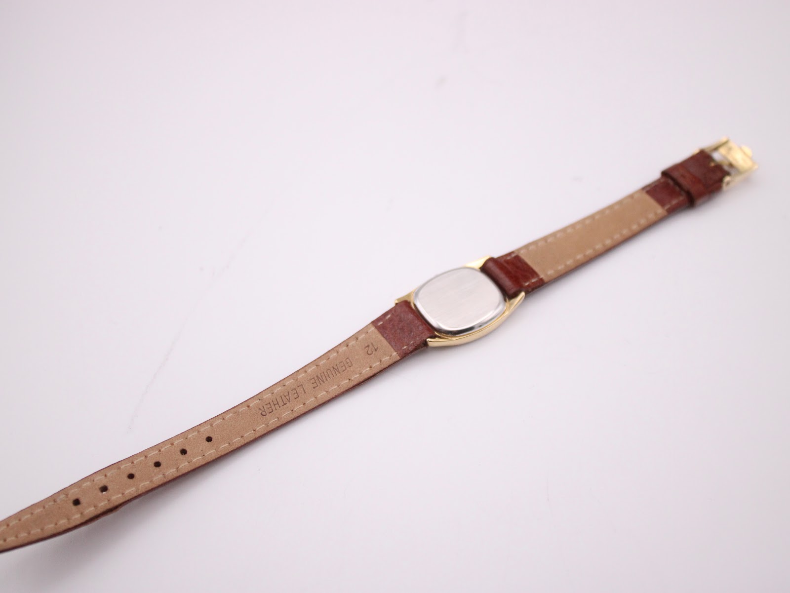 View of the watch from the back, showing the case back and the underside of the brown leather strap with "genuine leather" and "12" mark.