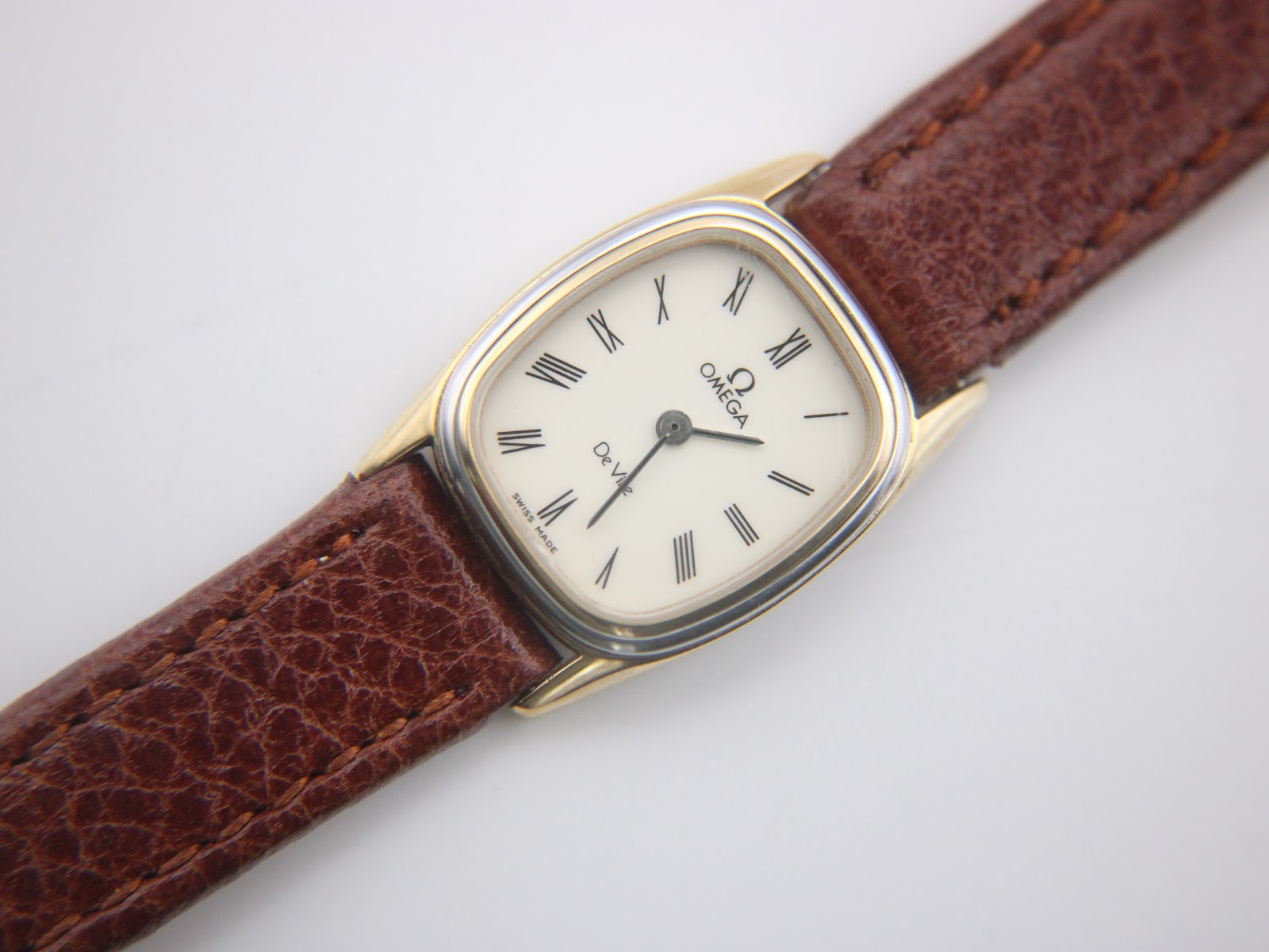 Close-up front view of the Omega De Ville cream dial with black Roman numeral and baton indices, and "Swiss Made" at 6 o'clock.