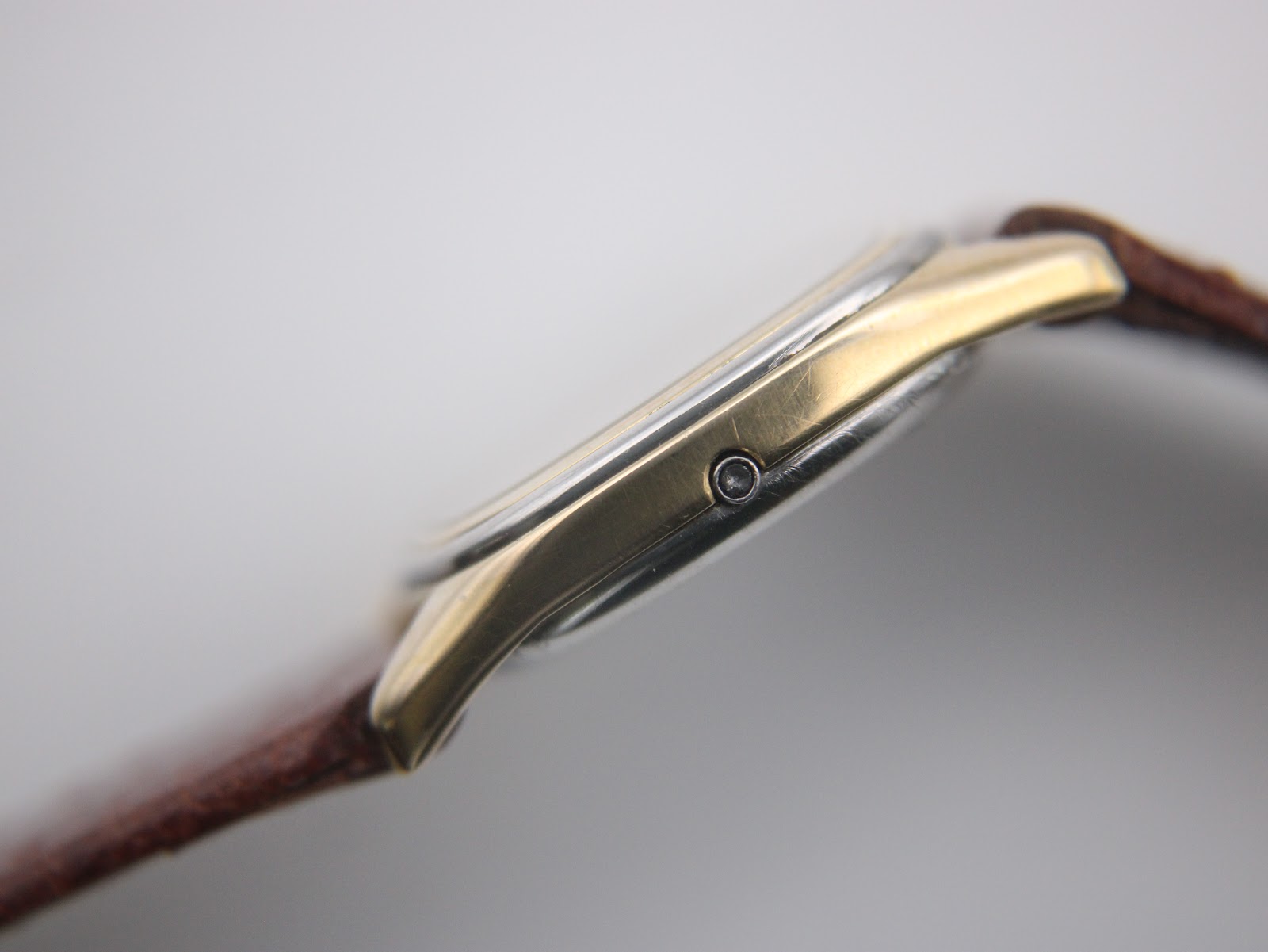 Close-up side profile of the Omega De Ville cushion case, showing the gold plating and crown.