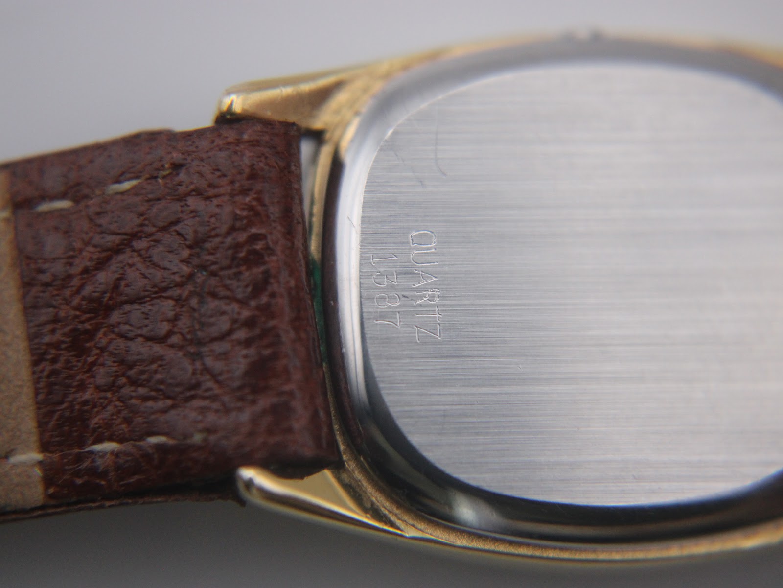 Close-up of the brushed stainless steel case back of the Omega De Ville, with "QUARTZ 1337" engraving.