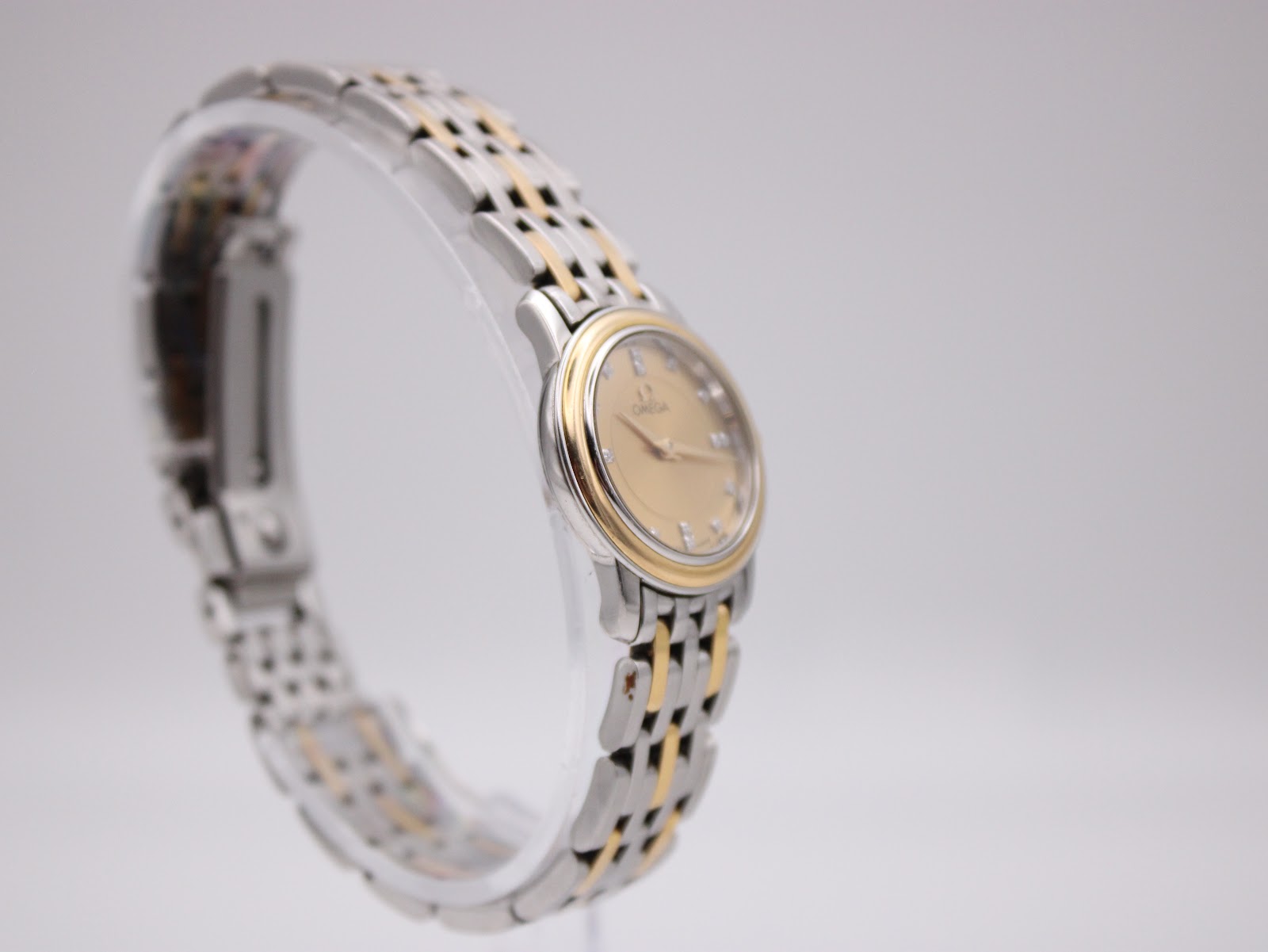 Opposite angled side view of the Omega watch on a display stand, showing the signed crown.