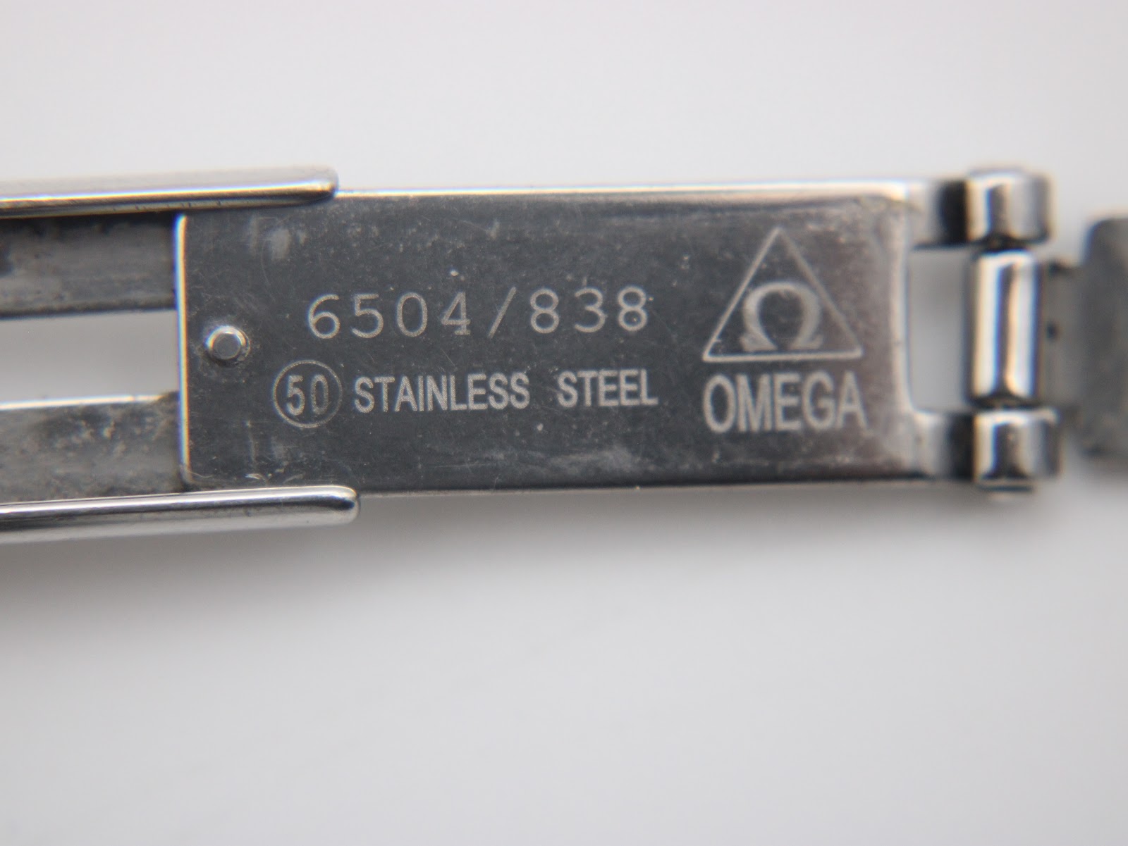 Interior view of the Omega bracelet clasp, showing "STAINLESS STEEL" and "OMEGA" engravings.