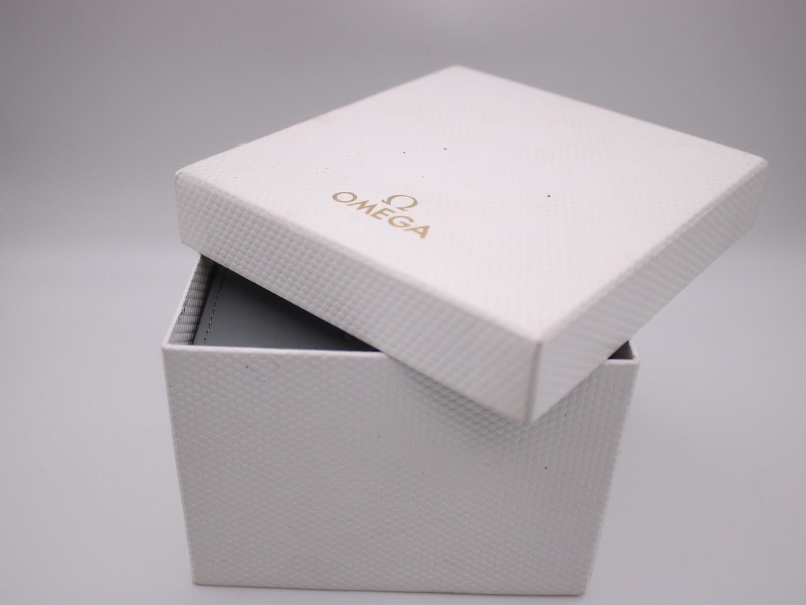 Opened white outer box with gold omega logo, part of the original packaging.