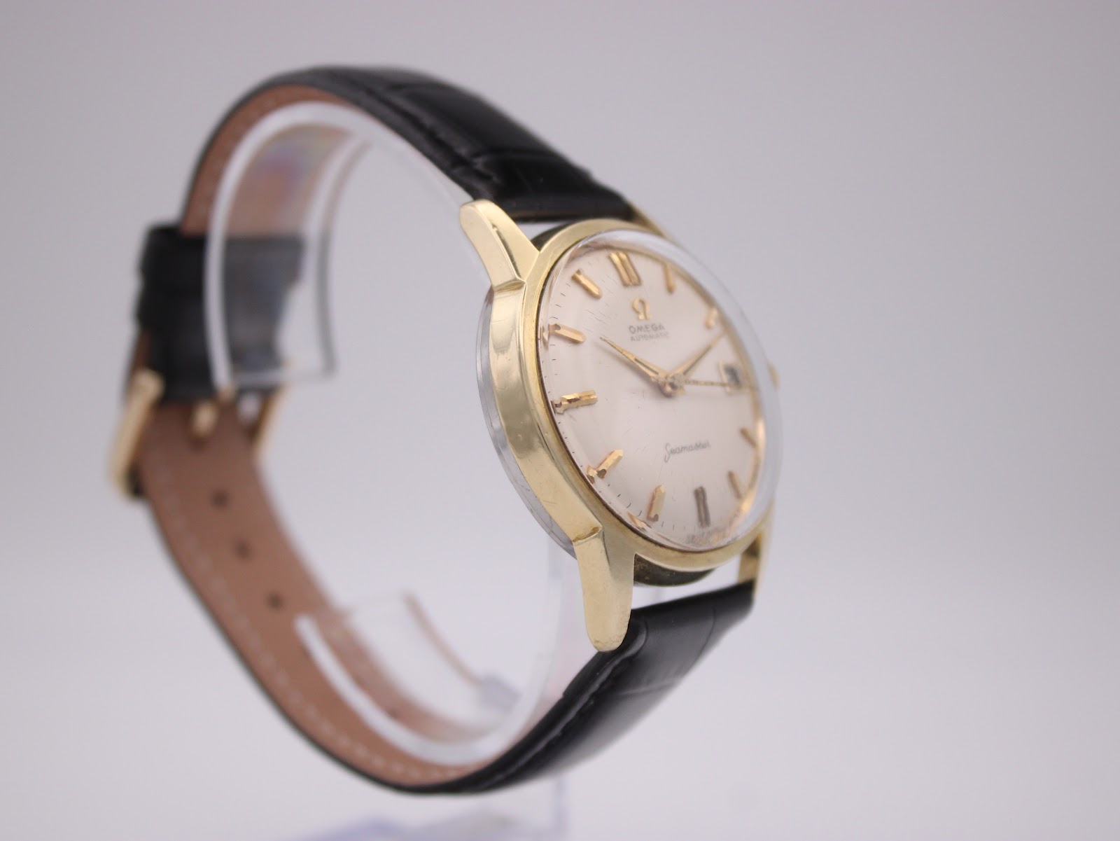 Angled side view of the omega seamaster watch, showing the gold-toned case and black leather strap.