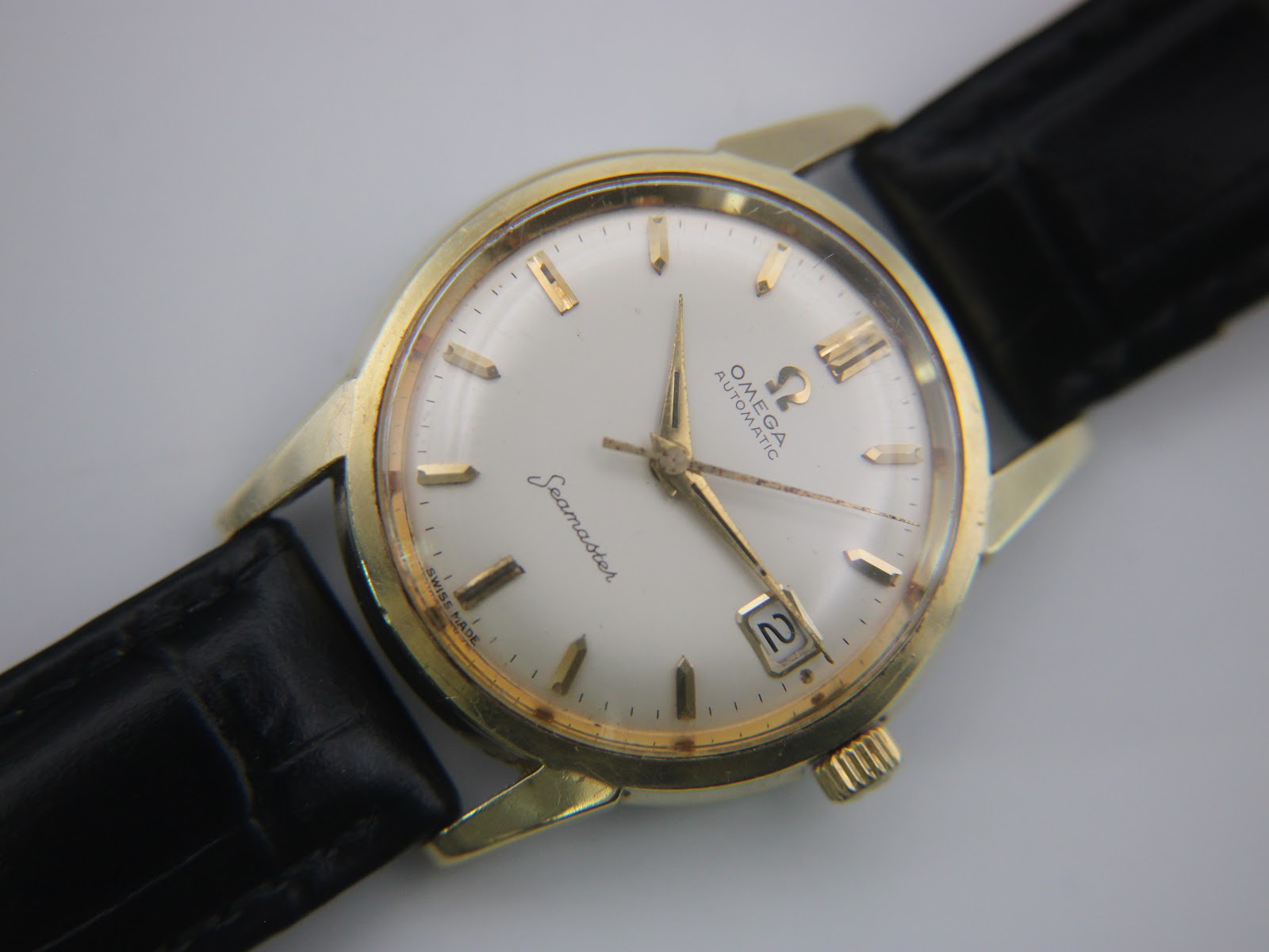 Close-up front view of the omega seamaster dial, showing cream colour, gold baton indices, and date window.