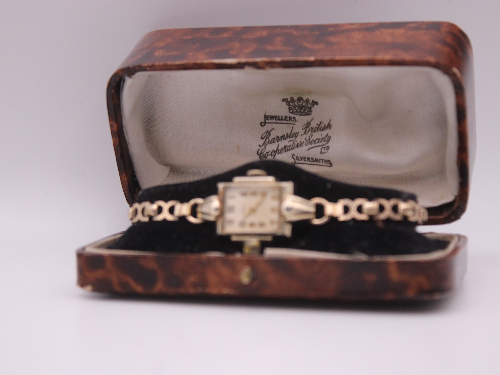 The vintage Omega watch placed inside its original brown faux tortoise shell box, open.