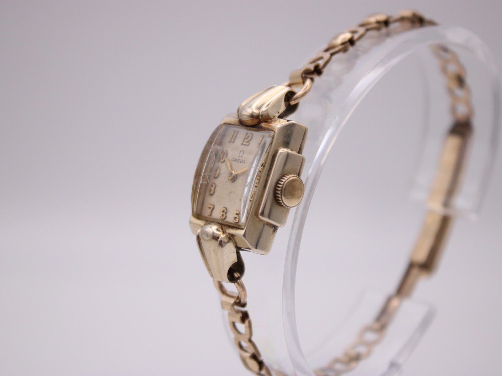 Angled side view of the Omega watch showing the rectangular case, crown, and bracelet on a display stand.