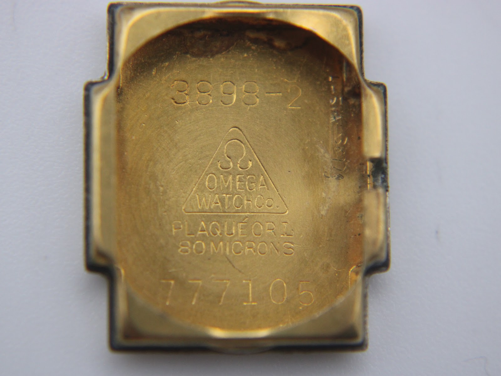 Close-up of the inside case back of the Omega watch, showing model number "3898-2", Omega logo, and "PLAQUÉ OR L 80 MICRONS" inscription.