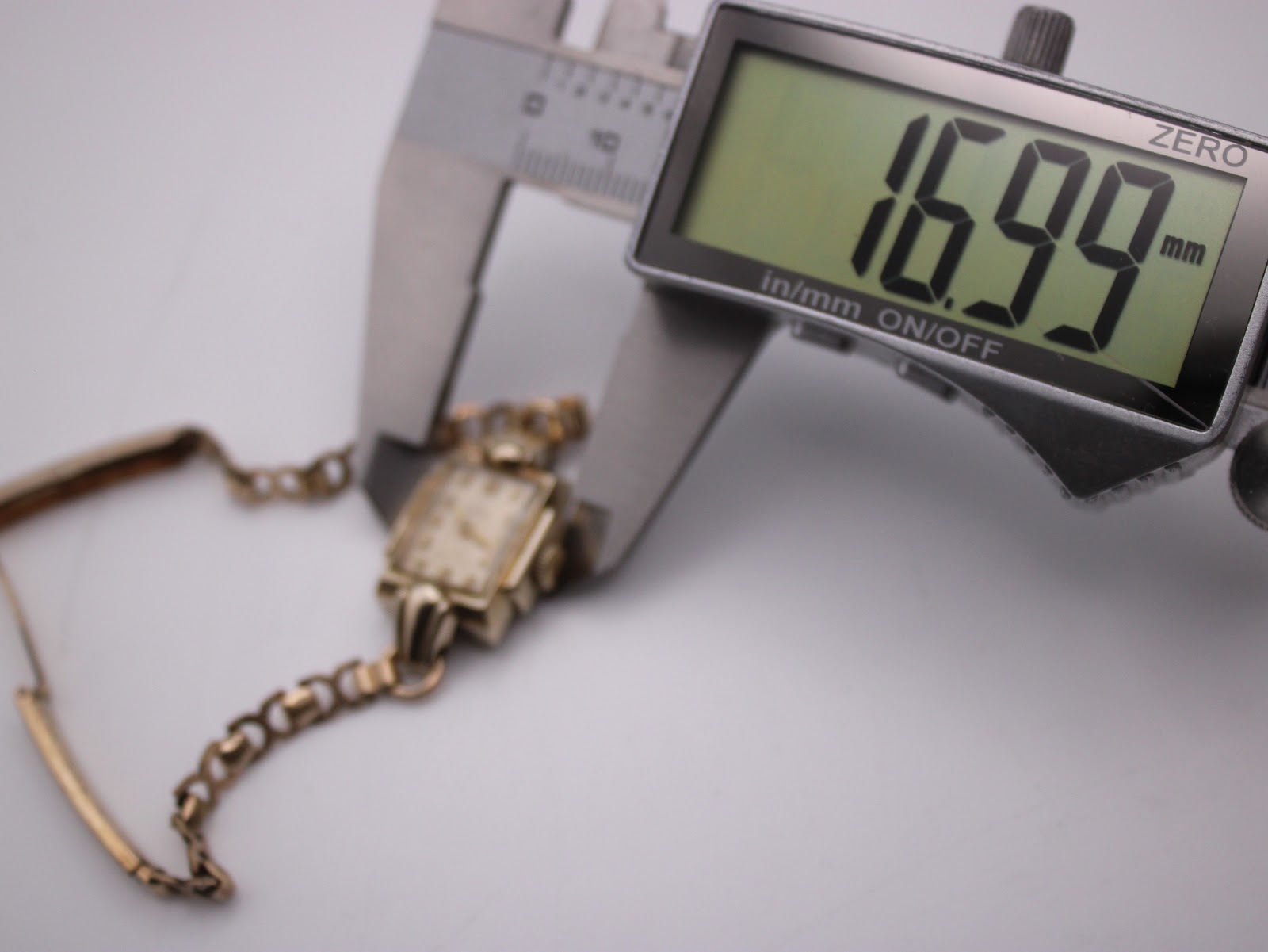 Digital caliper measuring the case diameter of the Omega watch, displaying 16.99mm.