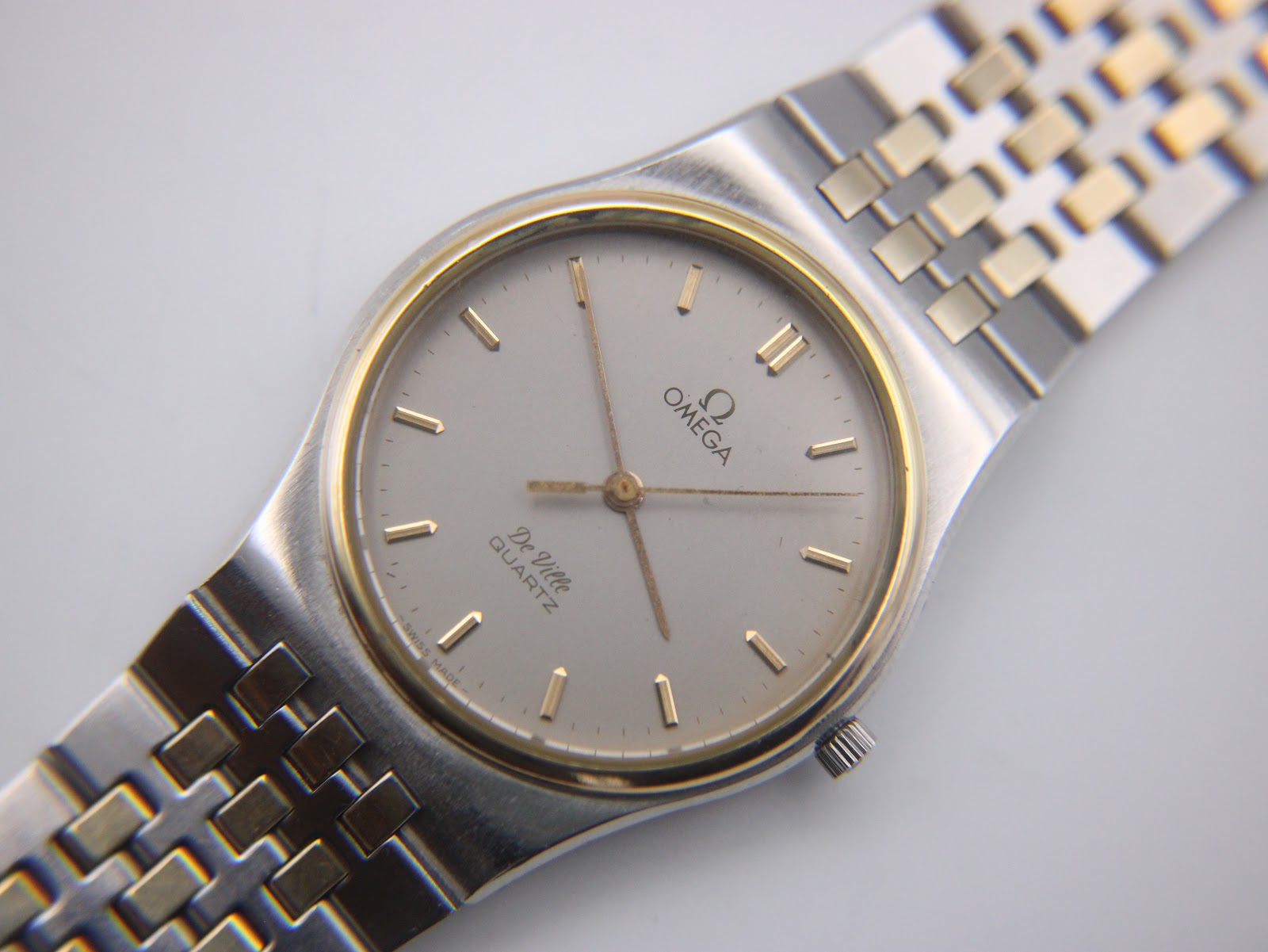 Close-up of the Omega De Ville dial, showing "OMEGA De Ville QUARTZ" text and gold baton indices.