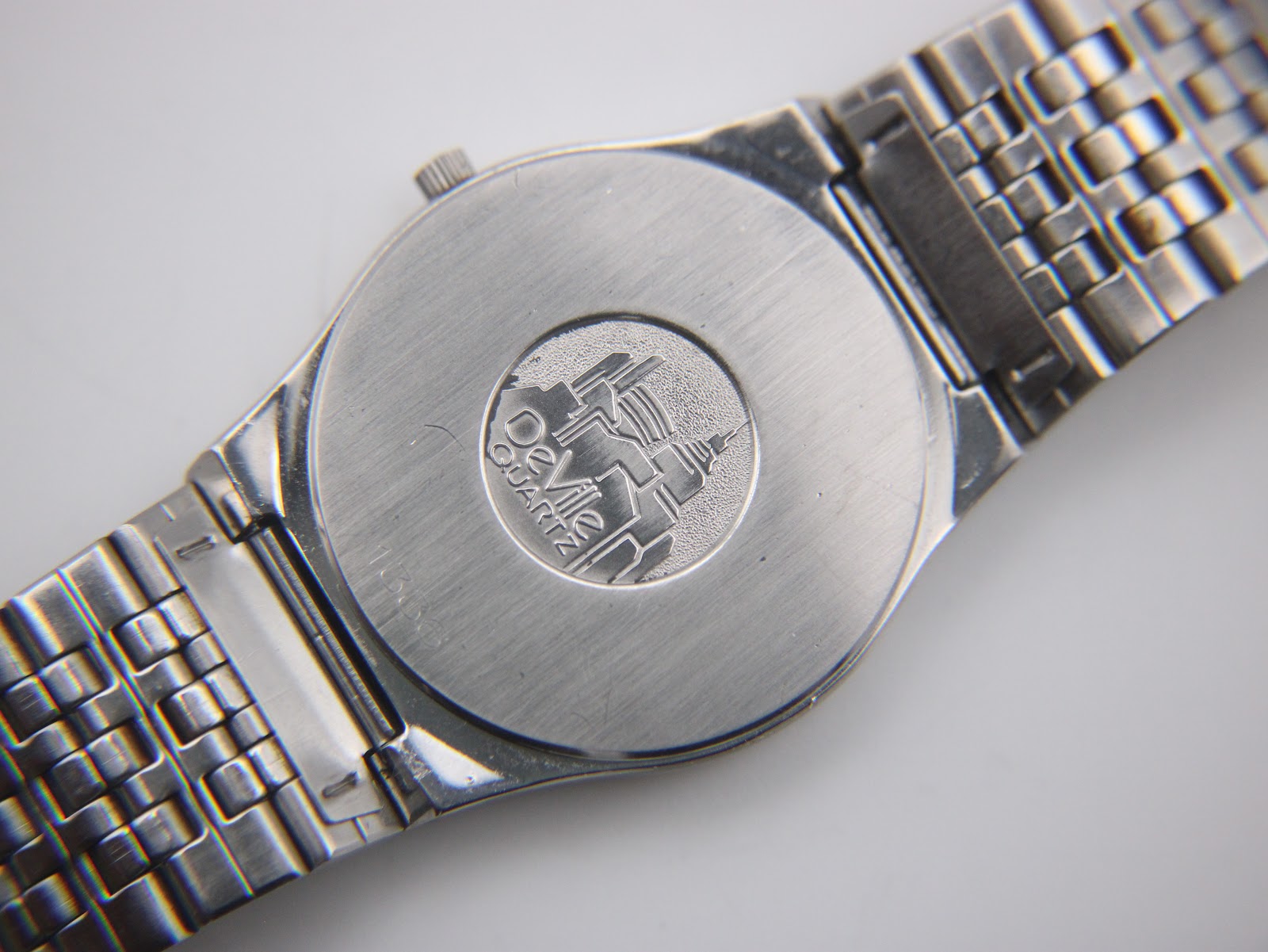 Close-up of the brushed stainless steel case back with the iconic De Ville building emblem and 'De Ville QUARTZ' text.