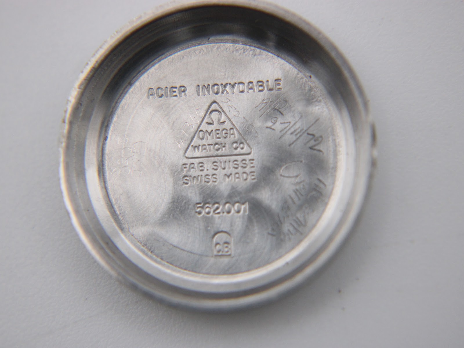 Inside view of the watch's stainless steel case back, engraved with 'ACIER INOXYDABLE OMEGA WATCH CO FAB. SUISSE SWISS MADE 562.001'.